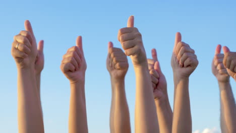 hands with thumbs up raised against blue sky