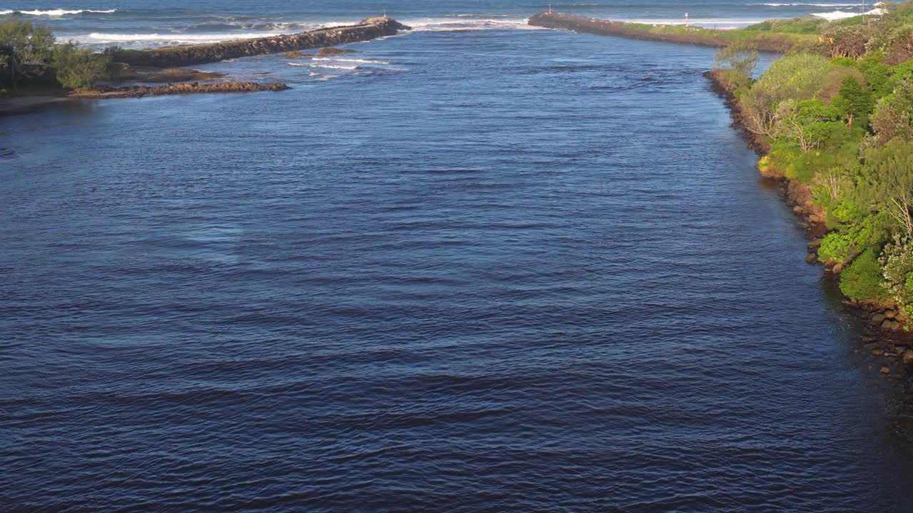 Drone footage captures the serene Brunswick Heads river inlet, showcasing lush greenery and calm waters under clear skies