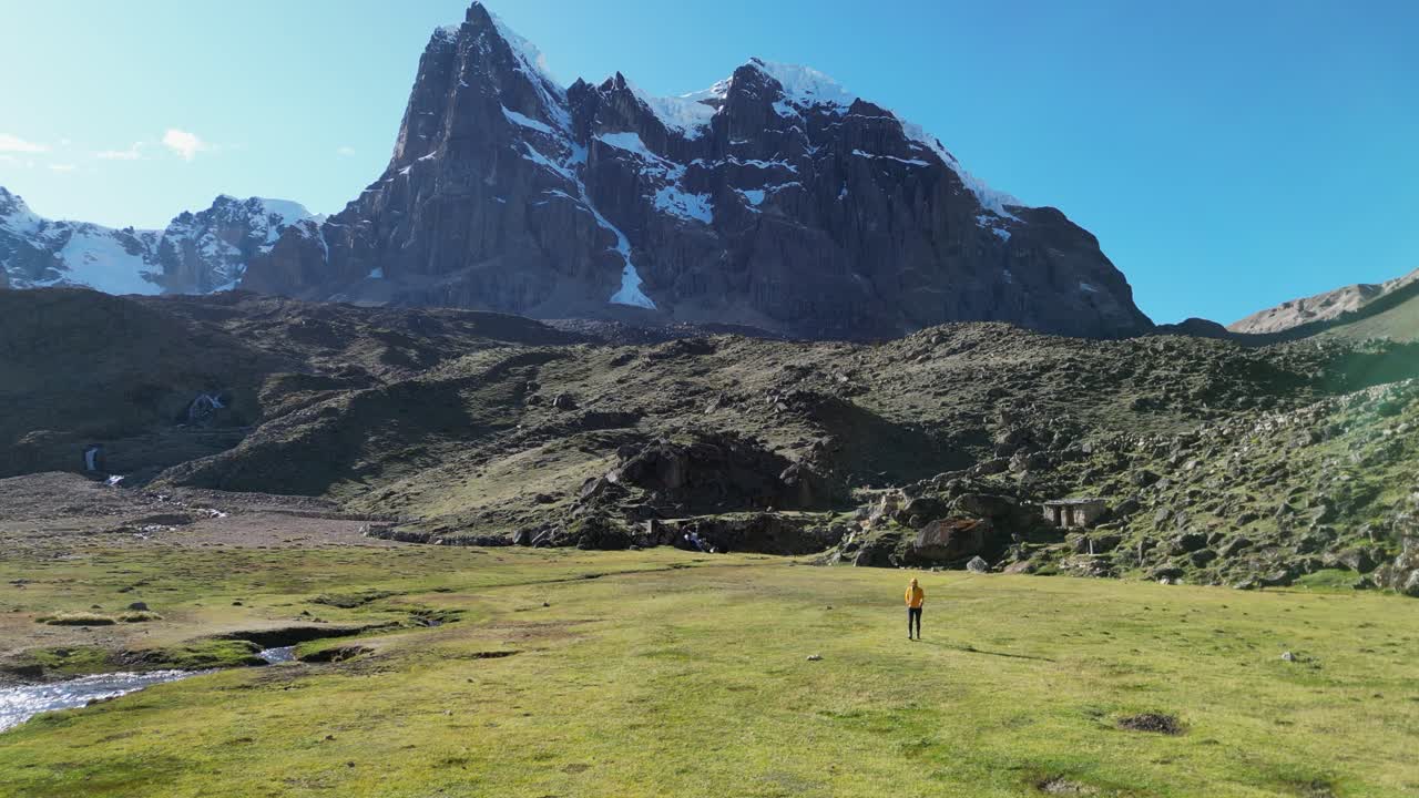 Flyover hiker walking on alpine meadow below rugged mountain peak, Peru