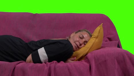 A tired beautiful blonde woman falls down, in slow motion, on the sofa, over a green screen