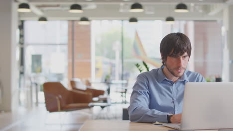 Businessman-And-Businesswoman-Having-Informal-Meeting-By-Desk-In-Modern-Open-Plan-Office