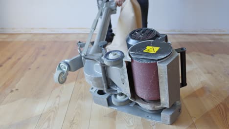 person is replacing the sandpaper roll on a floor sanding machine, showing the process clearly on a wooden parquet floor, tool and hands visible, static camera, for maintenance or setup