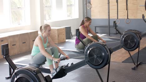 happy unaltered diverse women fist bumping after exercising on rowing machines at gym, slow motion