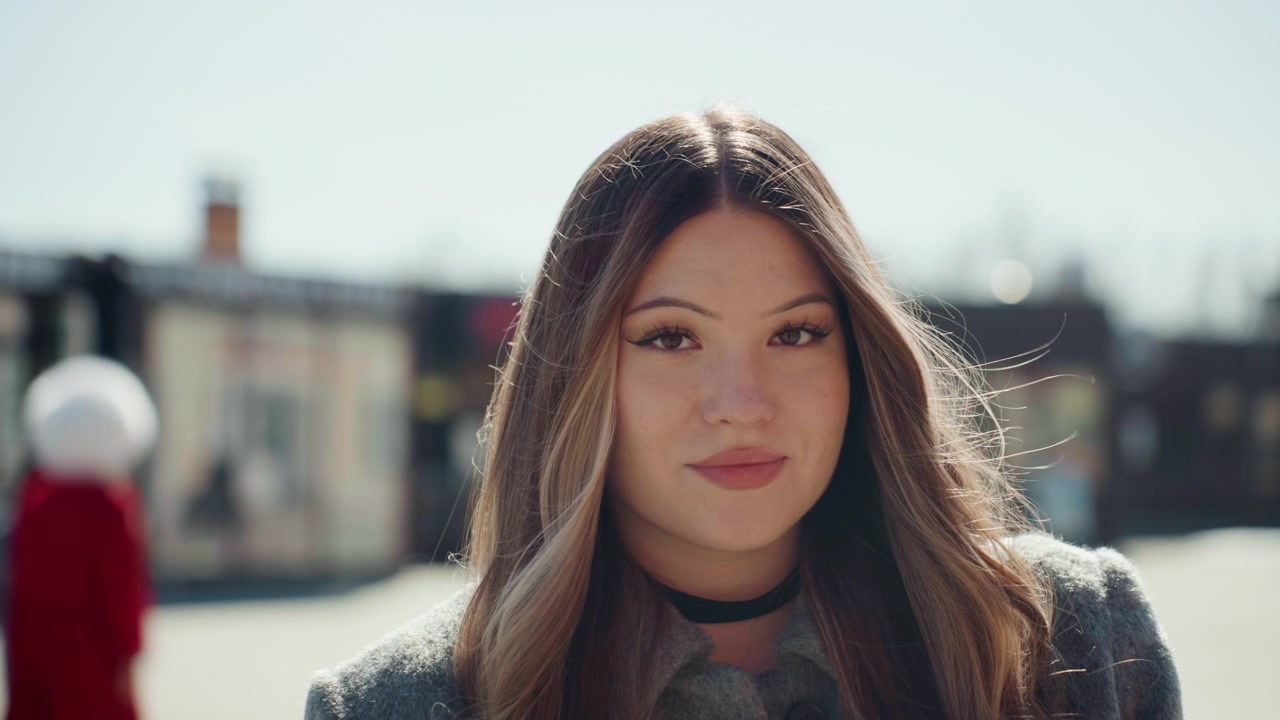 Scatto singolo luminoso con luce soffusa. Bella donna con illuminazione delicata e presenza sicura all'aperto. Affascinante signora ripresa in primo piano con sfondo urbano ed espressione naturale