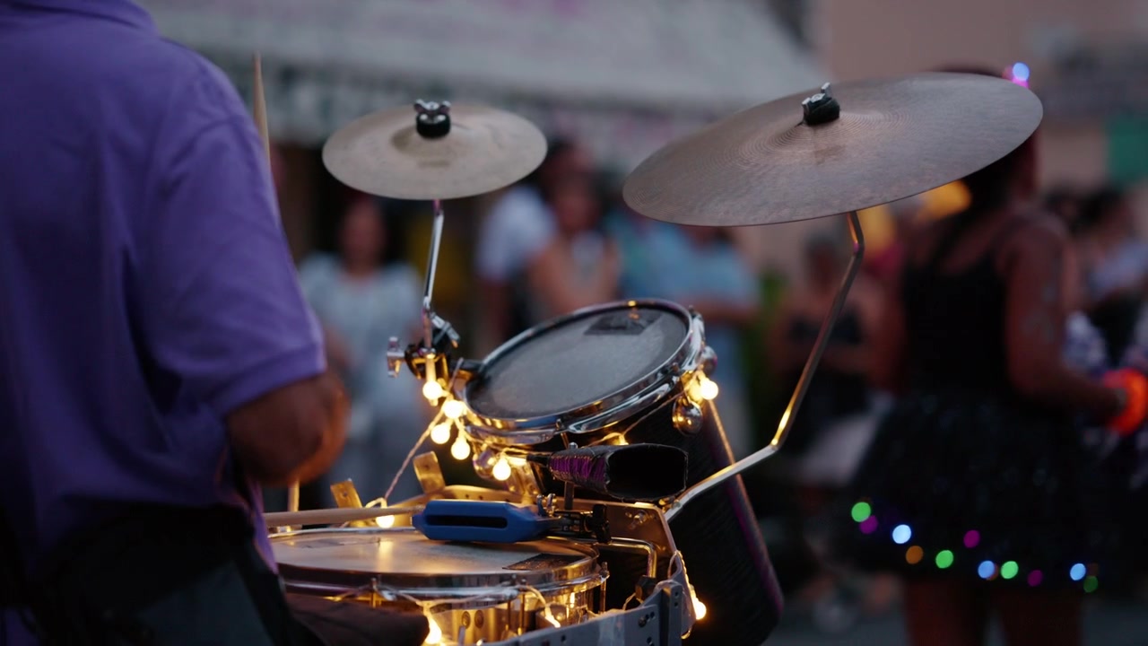Manos de músico golpeando tambores decorados con luces brillantes, creando ritmo y energía en un vibrante festival al aire libre por la noche.
