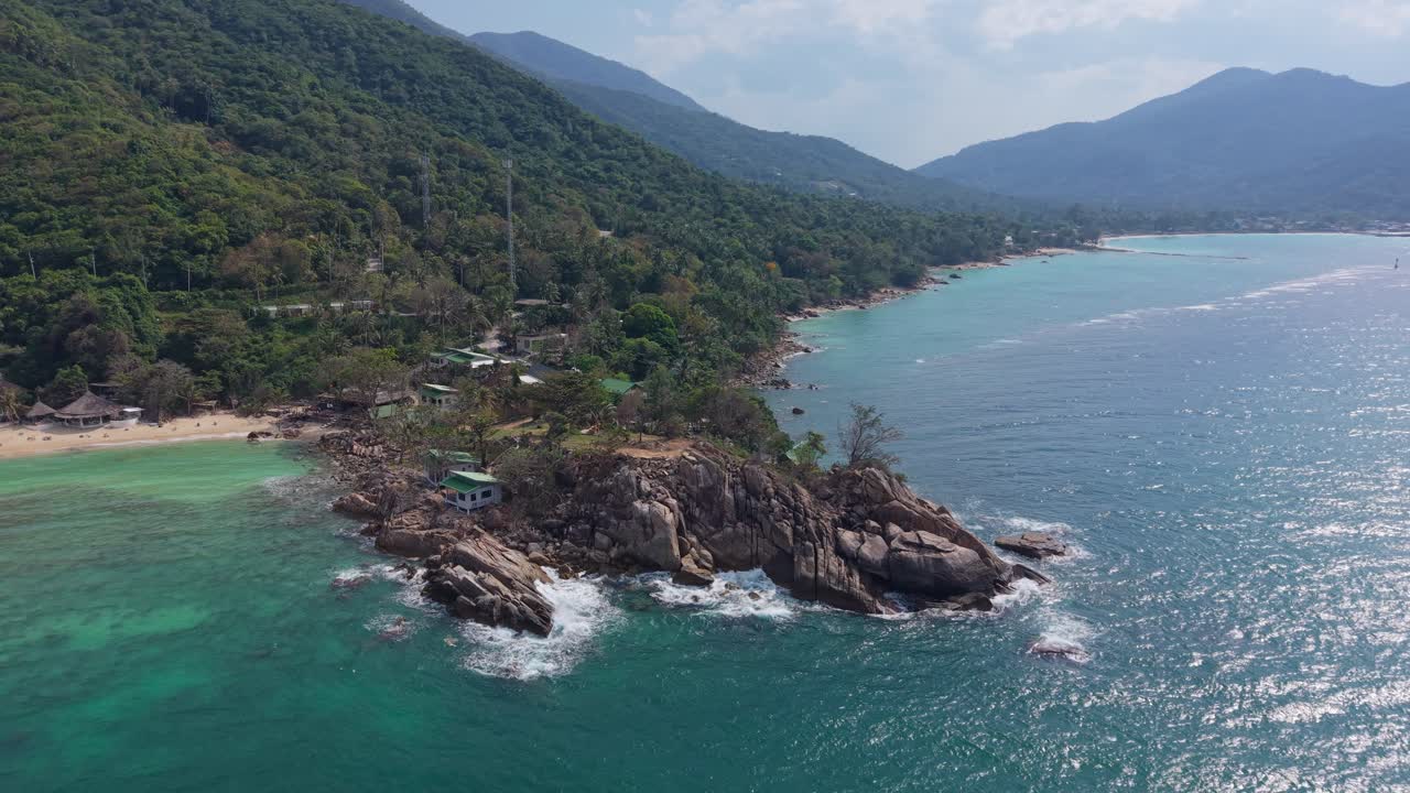Cinematic footage capturing ocean surf breaking along granite shoreline beneath lush hillside