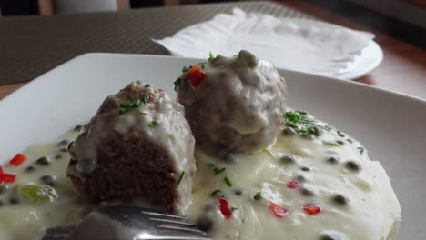 Adding-potatoes-to-a-plate-with-meatballs-and-white-sauce