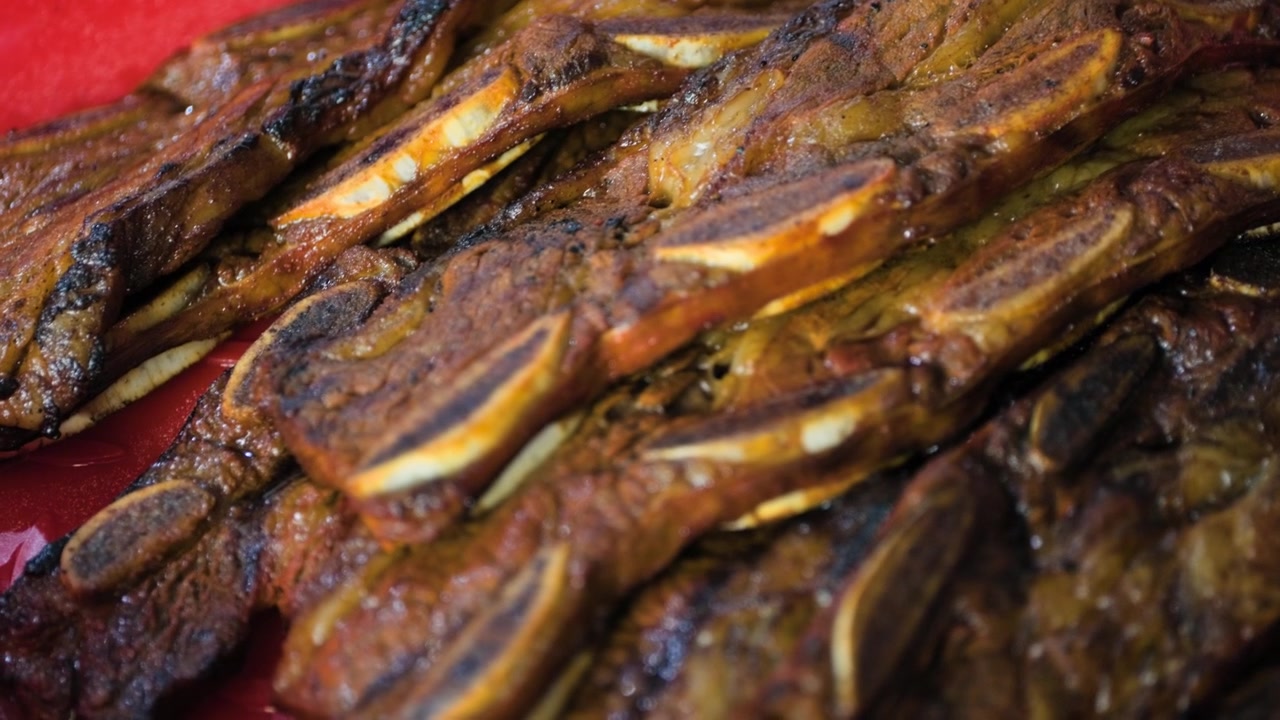 Primo piano di costine di manzo cotte e pronte su una griglia calda, durante la preparazione al barbecue.