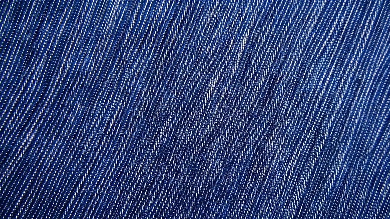 Makrovisning af indigoblå denim twill, der viser tætvævede tråde, diagonale riller, hvide nister og en rig tekstiltekstur med en diskret glans, naturlig struktur og robust industriel karakter