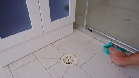 wiping bathroom shower floor with green cleaning cloth