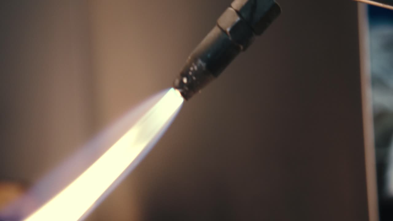 Close up footage of nozzle of blacksmith welding tool and gas flame heating a piece of metal, in industrial workplace
