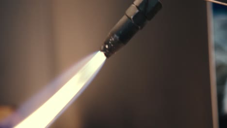 close up footage of nozzle of blacksmith welding tool and gas flame heating a piece of metal, in industrial workplace