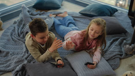 cute siblings using smartphones indoors. children giving high five.