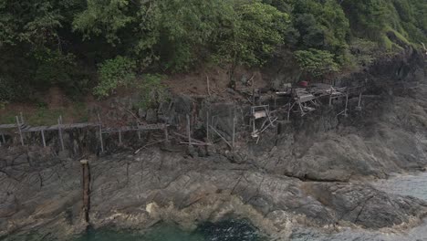 Toma-De-órbita-De-Camión-De-Drones,-Vista-De-Pájaro-De-Una-Tabla-De-Madera-Abandonada-Y-Cubierta-A-Lo-Largo-De-La-Costa-De-Roca-De-Granito-En-Una-Isla-Tropical-Con-Exuberante-Bosque-Verde-Y-Océano