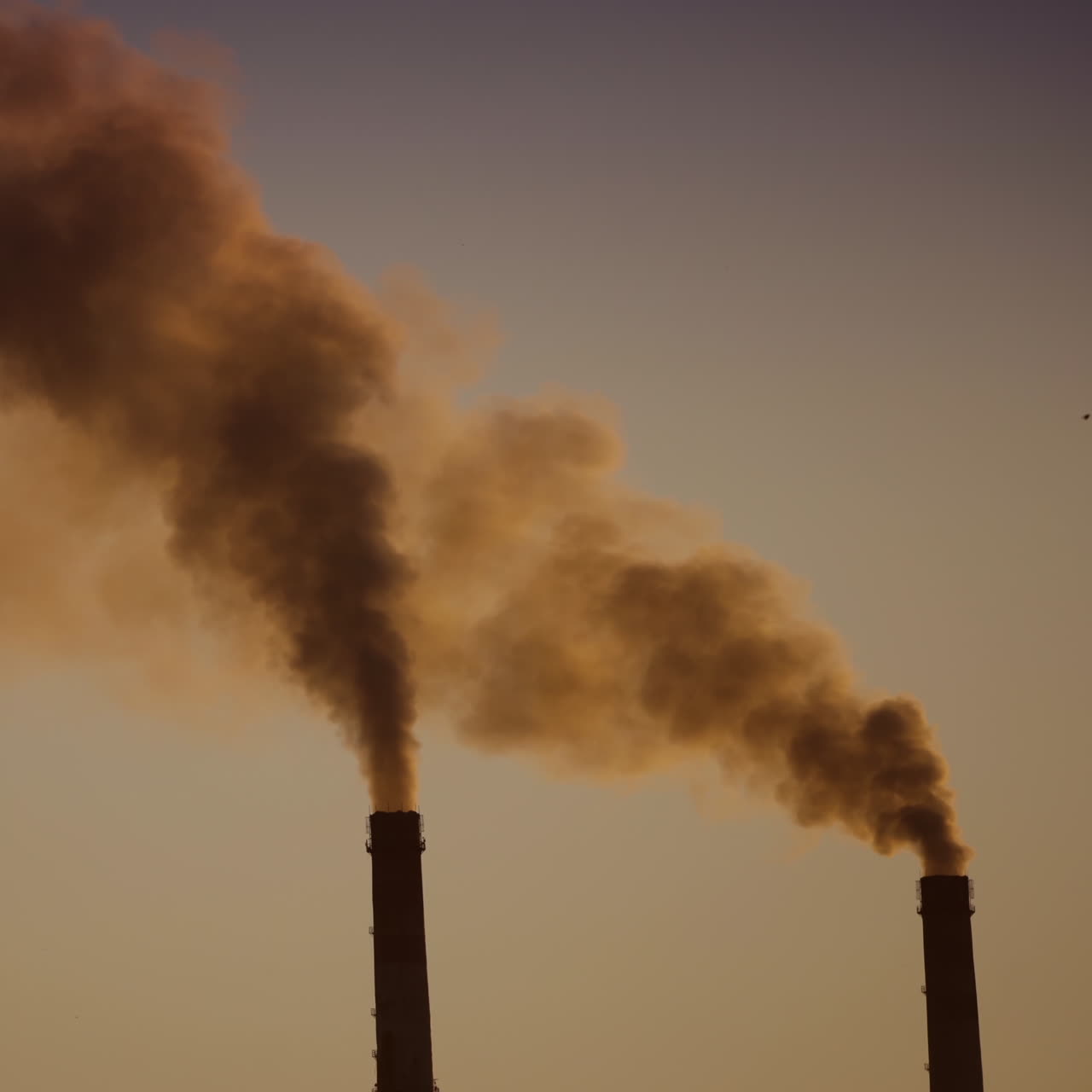 Dark smoke from pipes in the air at sunset. Two large pipes of industrial factory produce chemical smoke in the evening. Environmental pollution.