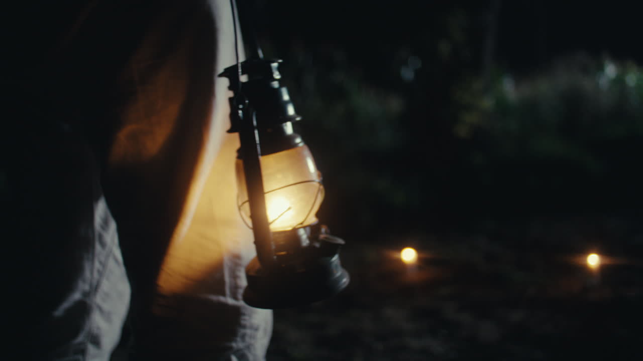 A person holding a lit vintage lantern in the dark