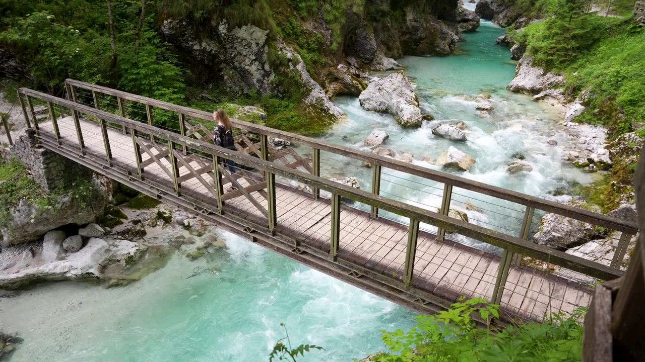 Viaggiatore avventuroso che attraversa un ponte di legno nel paesaggio delle Gole di Tolmin.