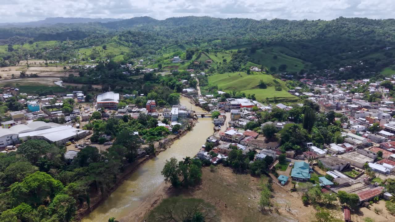 Imagem panorâmica de drone em torno de um vale de rio e da vila Crecida de Rio, dia ensolarado.