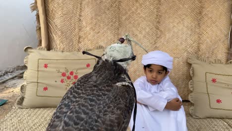 niño árabe en traje tradicional kandura mirando al halcón