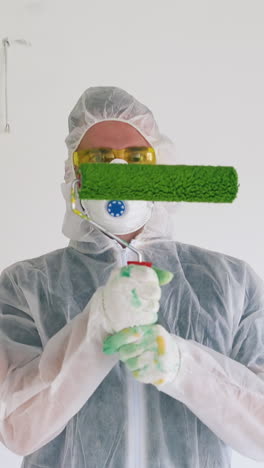 young family in goggles protective suits and masks holds rollers covered with green paint against white wall in empty room