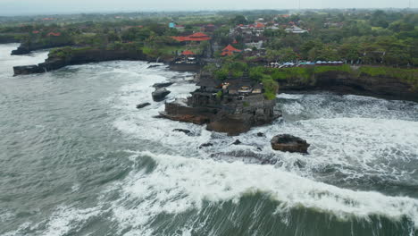 Wide-panoramic-view-of-Tanah-Lot-temple-in-dangerous-sea.-Strong-ocean-waves-crashing-into-rocks-around-famous-tourist-destination-in-Bali,-Indonesia