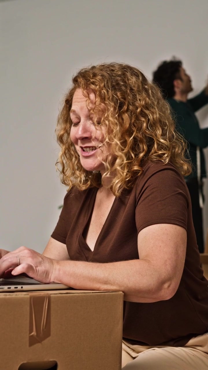 Donna che lavora al laptop mentre si appoggia a una scatola di cartone.