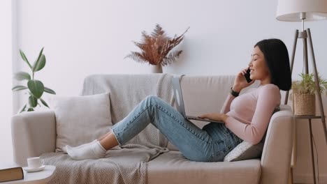 una mujer joven relajándose en el sofá usando una computadora portátil y un teléfono