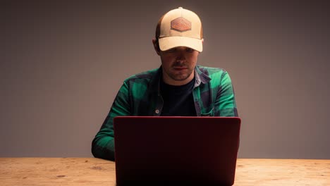 joven con sombrero trabaja en una computadora sobre un fondo gris
