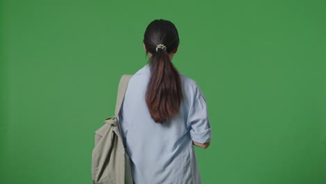 back view of asian teen girl student with a backpack walking in the green screen background studio