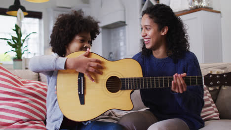 madre e hija de raza mixta sentadas en el sofá tocando la guitarra