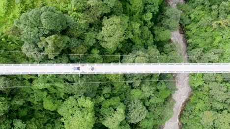 stunning top-down aerial footage of a pedestrian suspension bridge spanning a river in the himalayas. captures the dramatic view of the bridge amidst rugged terrain and rushing waters.