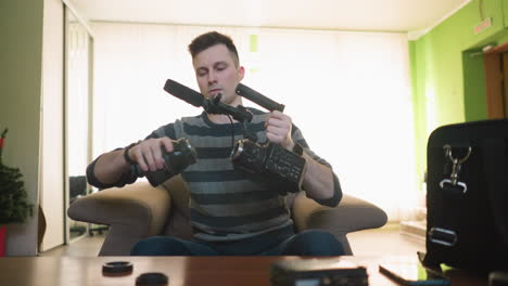person assembling video camera, attaching microphone and lens. indoor workspace with camera gear, bags, and tech tools. professional setup for video production and filming