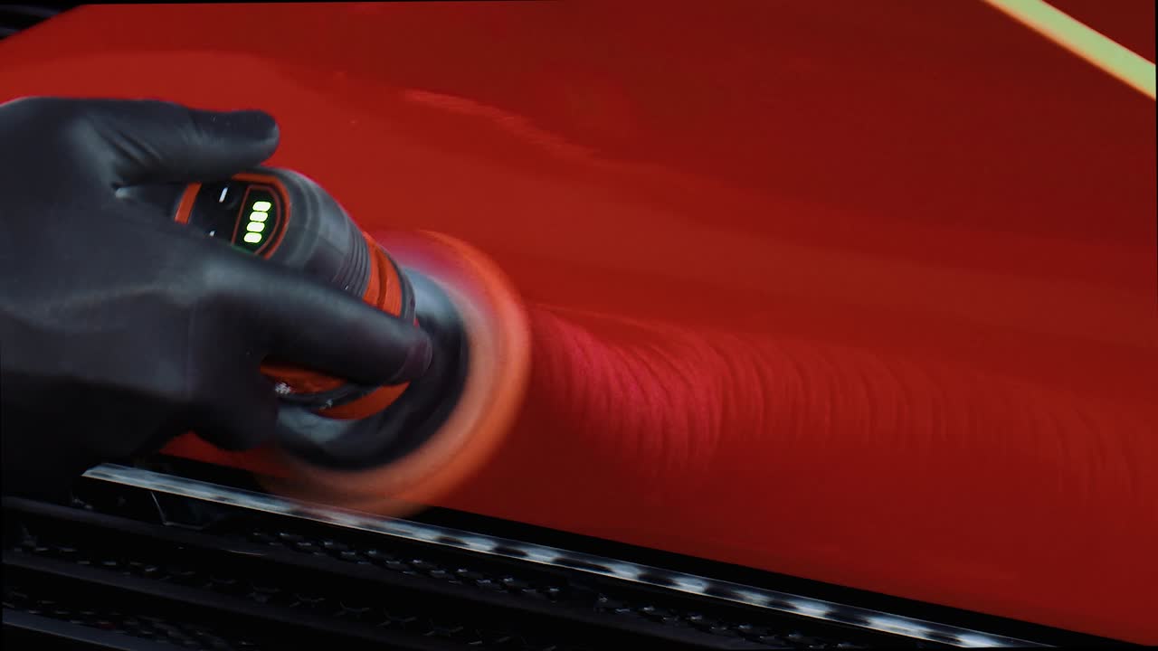 Close up of man with black latex gloves polishing red paint on car with a small polishing machine.
