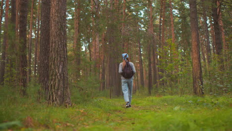 vista posterior de una mujer joven caminando por un sendero pacífico del bosque, con mochila y bandana azul, sosteniendo correas mientras camina en medio de vegetación exuberante y árboles altos