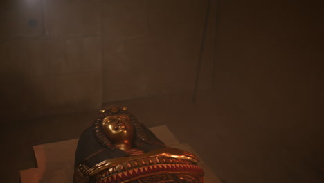 a golden mummy sarcophagus laying in a chamber in a tomb in the pyramids in a beam of light