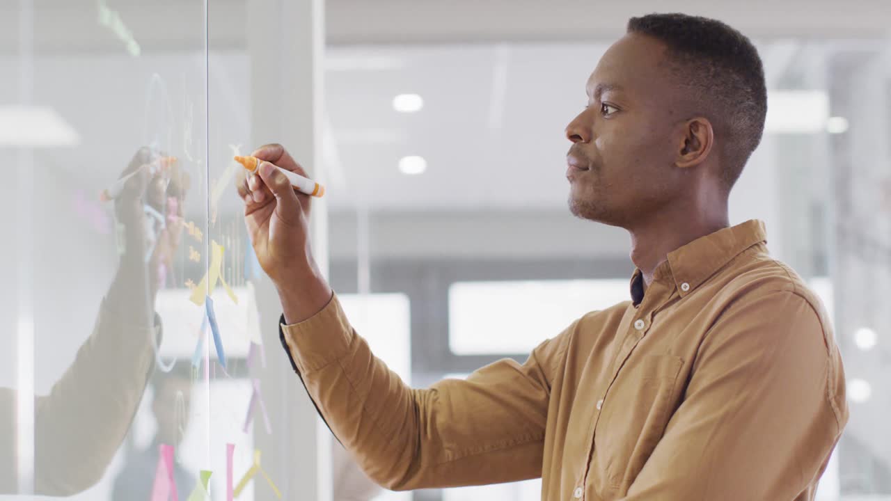 African american businessman writing on glass blackboard at office, slow motion