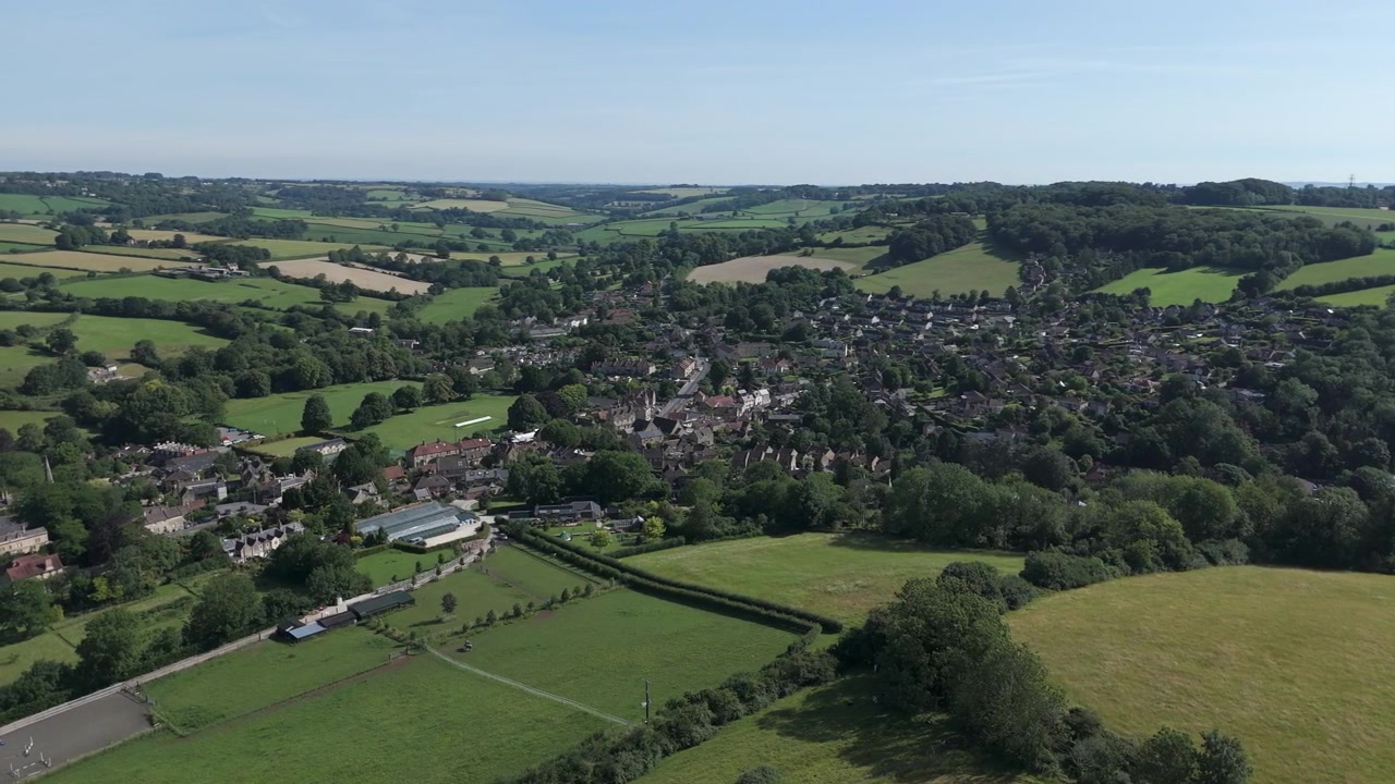 Aerial descend, pivot left - vista of Box from Ashley, Wiltshire on a summers day