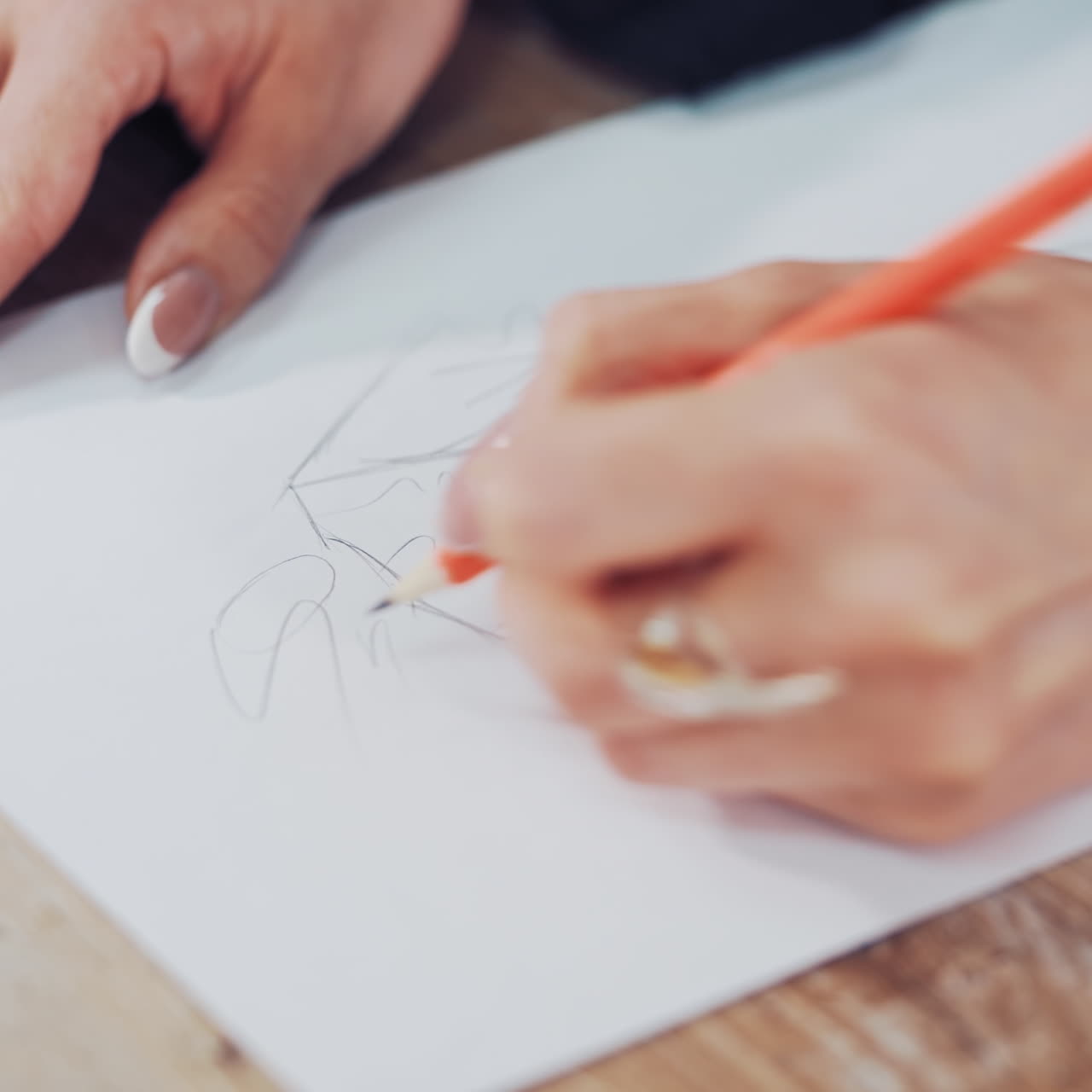 Young woman's hands of a fashion designer drawing sketches of clothes in the atelier. Female tailor draws with a sharp pencil indoors. Close-up
