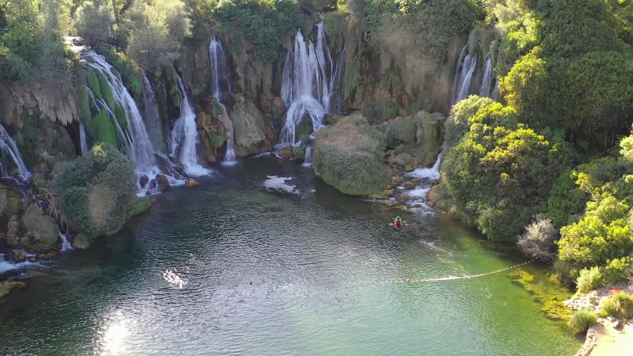 Kravica Waterfalls in Bosnia and Herzegovina with people on canoes getting close below, Aerial dolly out shot