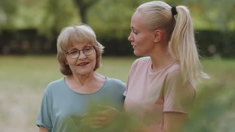 portrait of cheerful elderly woman and female trainer with smartphone