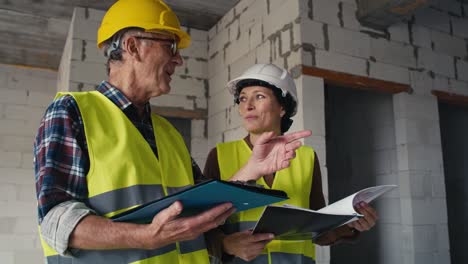 video estático de ángulo bajo de ingenieros caucásicos masculinos y femeninos hablando en el sitio de construcción.