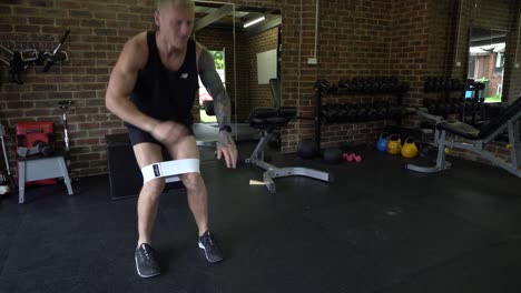 Tattooed-man-in-home-gym-squat-walk-with-resistance-bands-and-finish