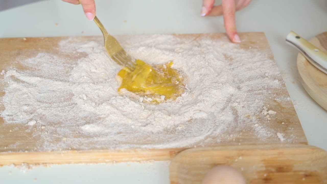Woman wearing an apron, breaking and mixing an egg in flour on a wooden cutting board in the kitchen