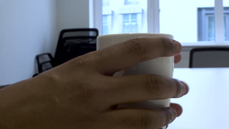 Close-Up-View-Of-Ethnic-Minority-Hands-Tapping-On-White-Mug-On-Table-In-Office-Meeting-Room