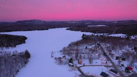 órbita-Aérea-Alrededor-De-Un-Pequeño-Pueblo-En-La-Orilla-De-Un-Lago-Congelado-Durante-Un-Amanecer-Increíble