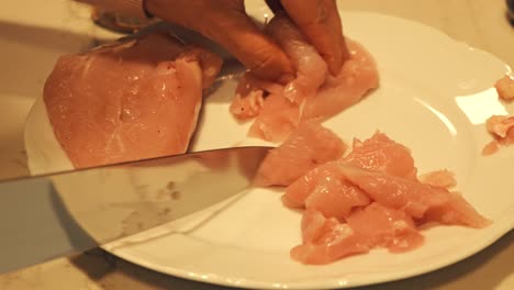 close-up of hands cutting raw meat on a white plate with a knife. food preparation in progress. focus on the cutting action.