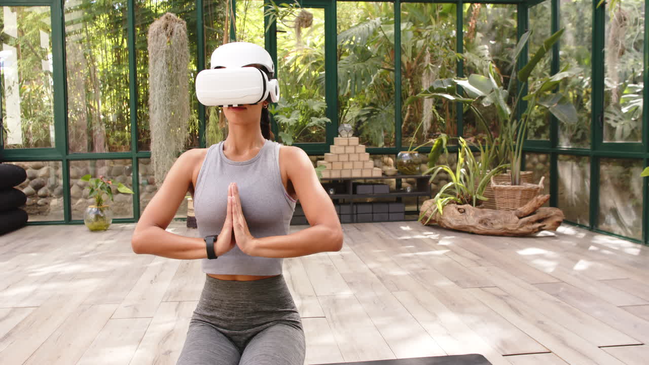 Practicing yoga with VR headset, woman meditating in glass house, copy space