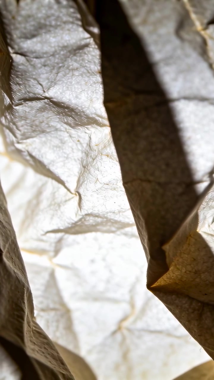 Vertical video: Shifting phone showing crumpled translucent paper in bag, capturing backlight folds