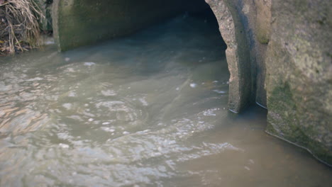 Close-view-of-water-flowing-fast-out-of-large-sewage-pipe-outdoors