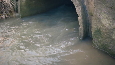 close view of water flowing fast out of large sewage pipe outdoors